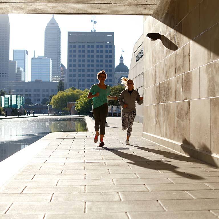 Two people jogging under a bridge along the canal in downtown Indianapolis. 